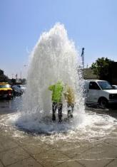 two Cerritos plubers get a shower beneath the spray of a broken water main